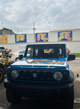 Blue SUV with a cartoon design on the hood in a parking lot with a store in the background.